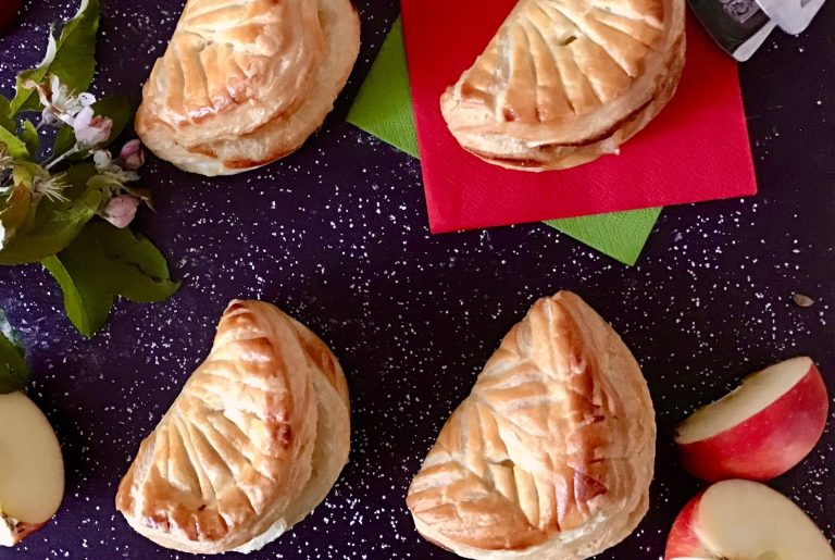 Blätterteig, Chaussons aux Pommes Gebackene Apfeltaschen auf einem dunklen Untergrund mit frischen Äpfeln.