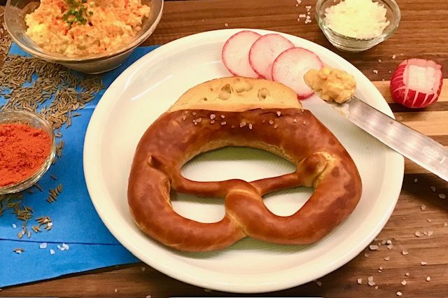 Brezeln und Laugengebäck Brezel mit Senf, Radieschen und Gewürzen auf einem weißen Teller.